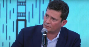 Moro é constrangido no Pânico. Ele usa terno preto, pelo branca e cabelos pretos e tem olhar confuso.