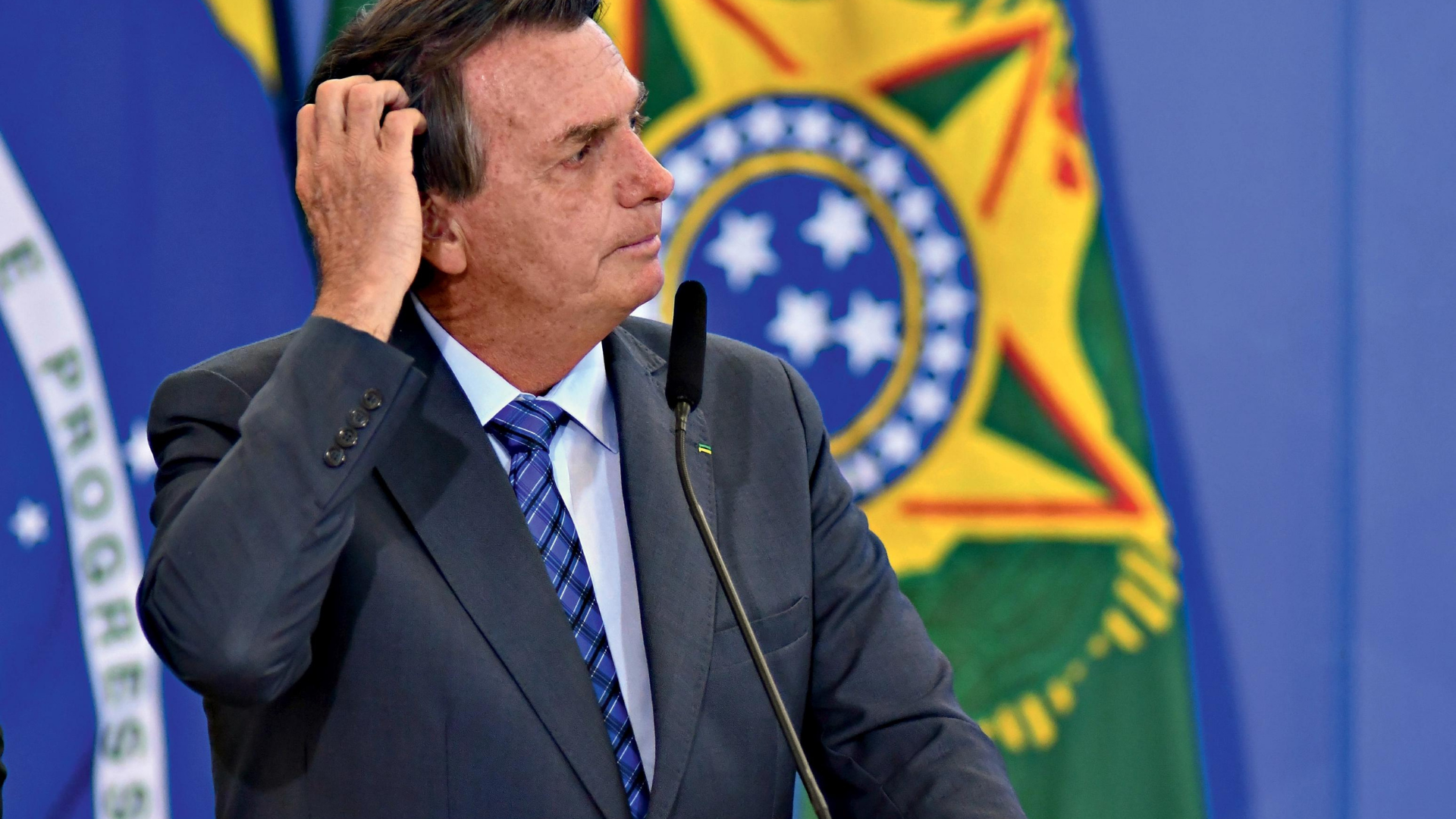 Ex-ministro de Bolsonaro abandona cargo no TSE. O presidente olha para o lado direito com a mão na cabeça e aaparência de estar preocupado.