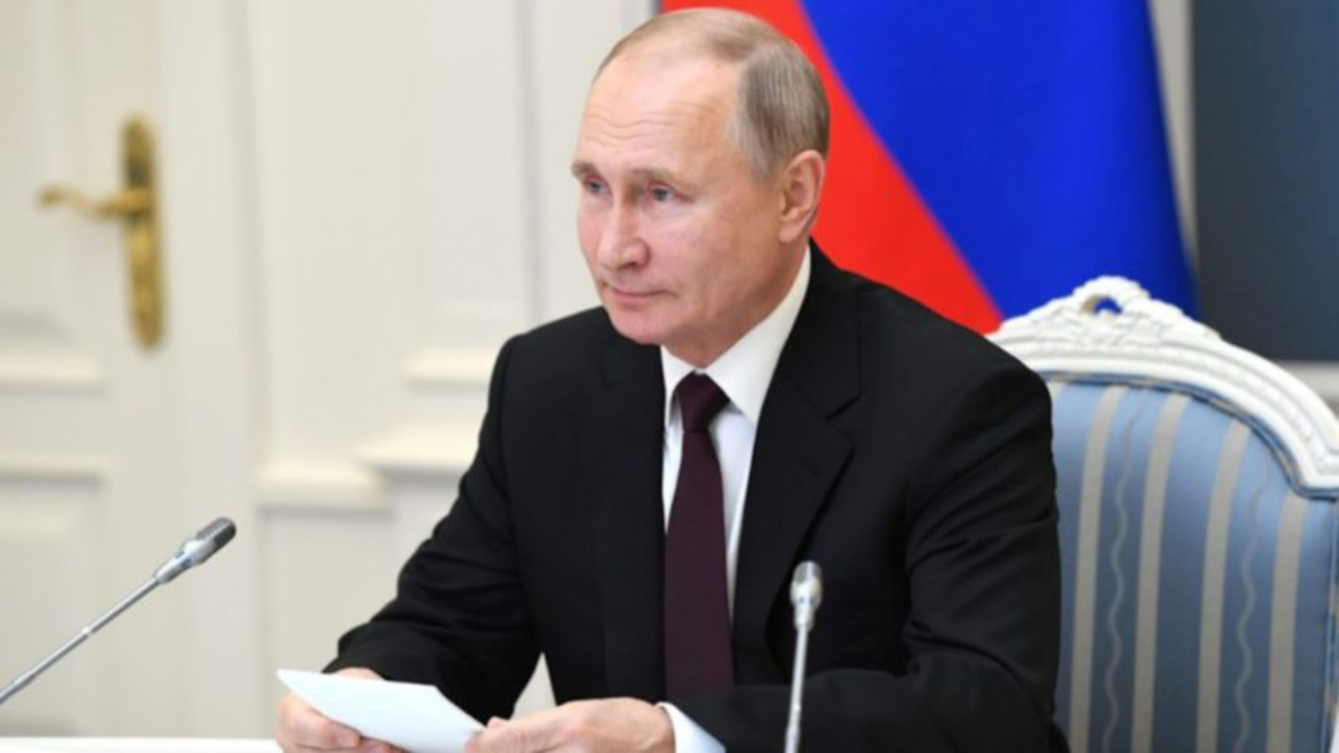 Rússia autoriza envio de tropas para 'manter a paz' em regiões de conflito na Ucrânia. Foto de Putin em uma cadeira, assinando um documento. Ele usa terno preto, tem pele branca e é calvo. O fundo está desfocado.
