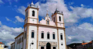 Foto da igreja deSanto Amato da Purificação. Ela é branca com cores em dourado e janeças azuis. tem suas torres.