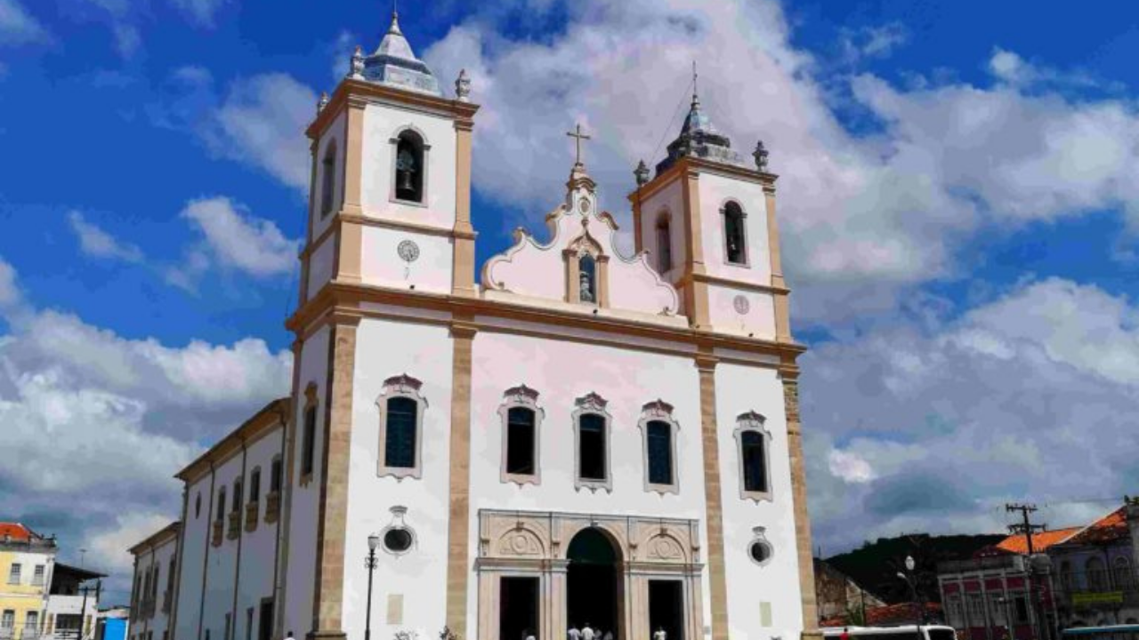Foto da igreja deSanto Amato da Purificação. Ela é branca com cores em dourado e janeças azuis. tem suas torres.