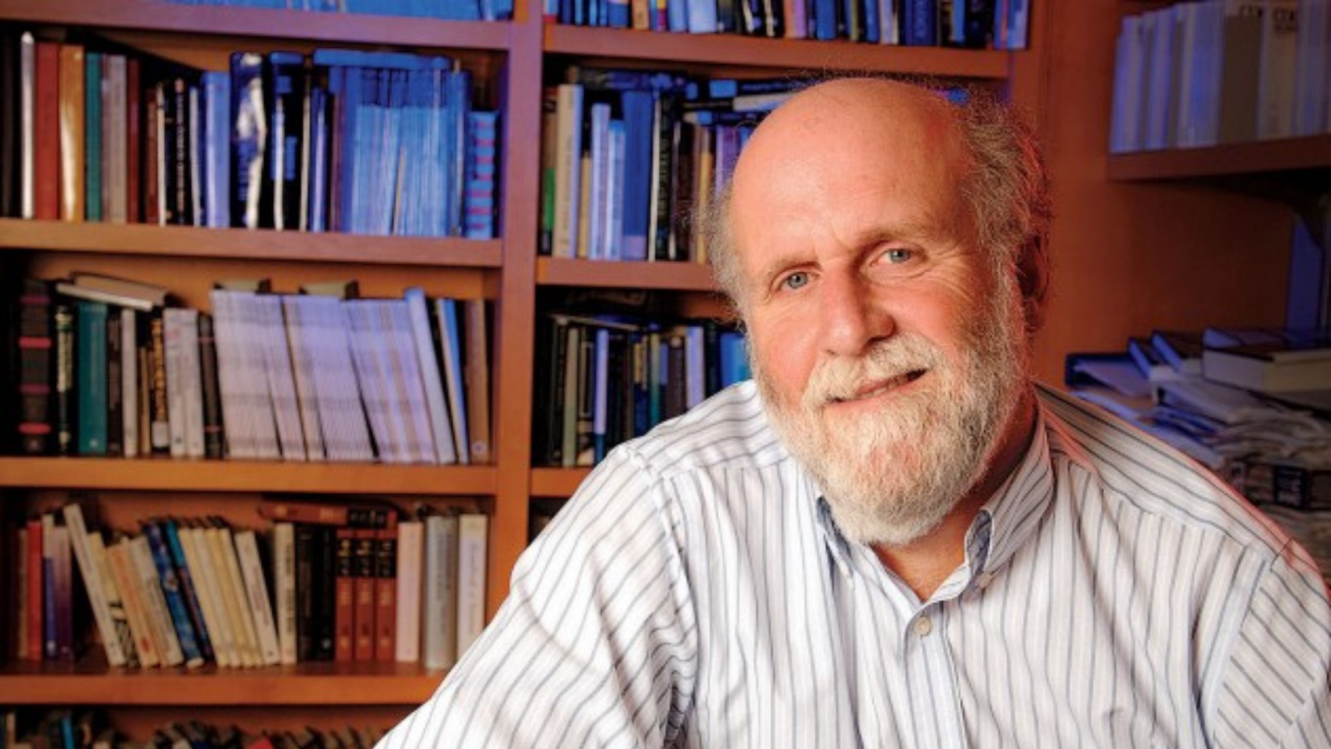 Fake news produz falsas memórias. O professor de Harvard está com uma camisa branca, com olhar sério e estante de livros atrás. 