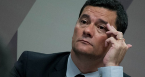 Foto de Sergio Moro com terno preto, mão esquerda na sombrancelha e olhar de preocupação