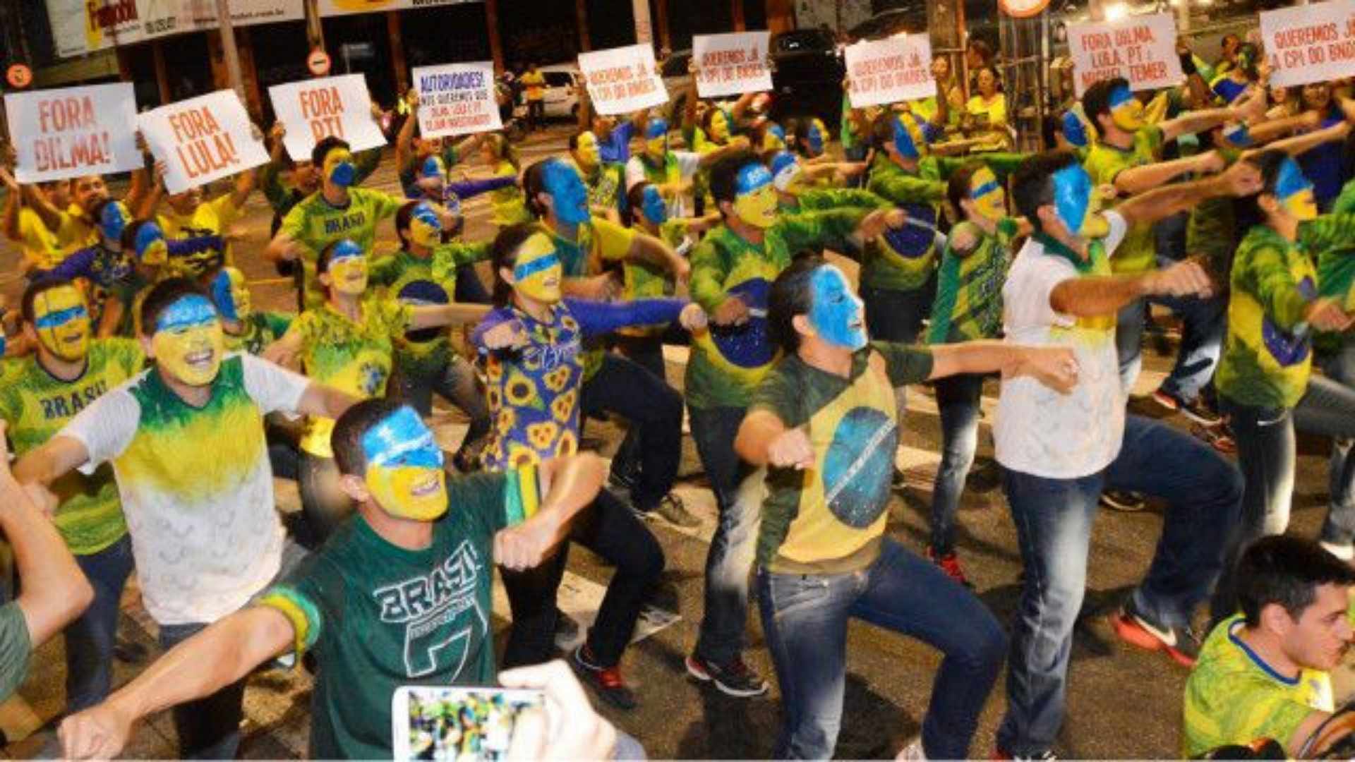 Responsável pela Dança Fora Dilma confessa ter se arrependendido. Na foto, pessoas pintadas de verde e amarelo fazem dança na rua com cartazes escritos "Fora Lula".