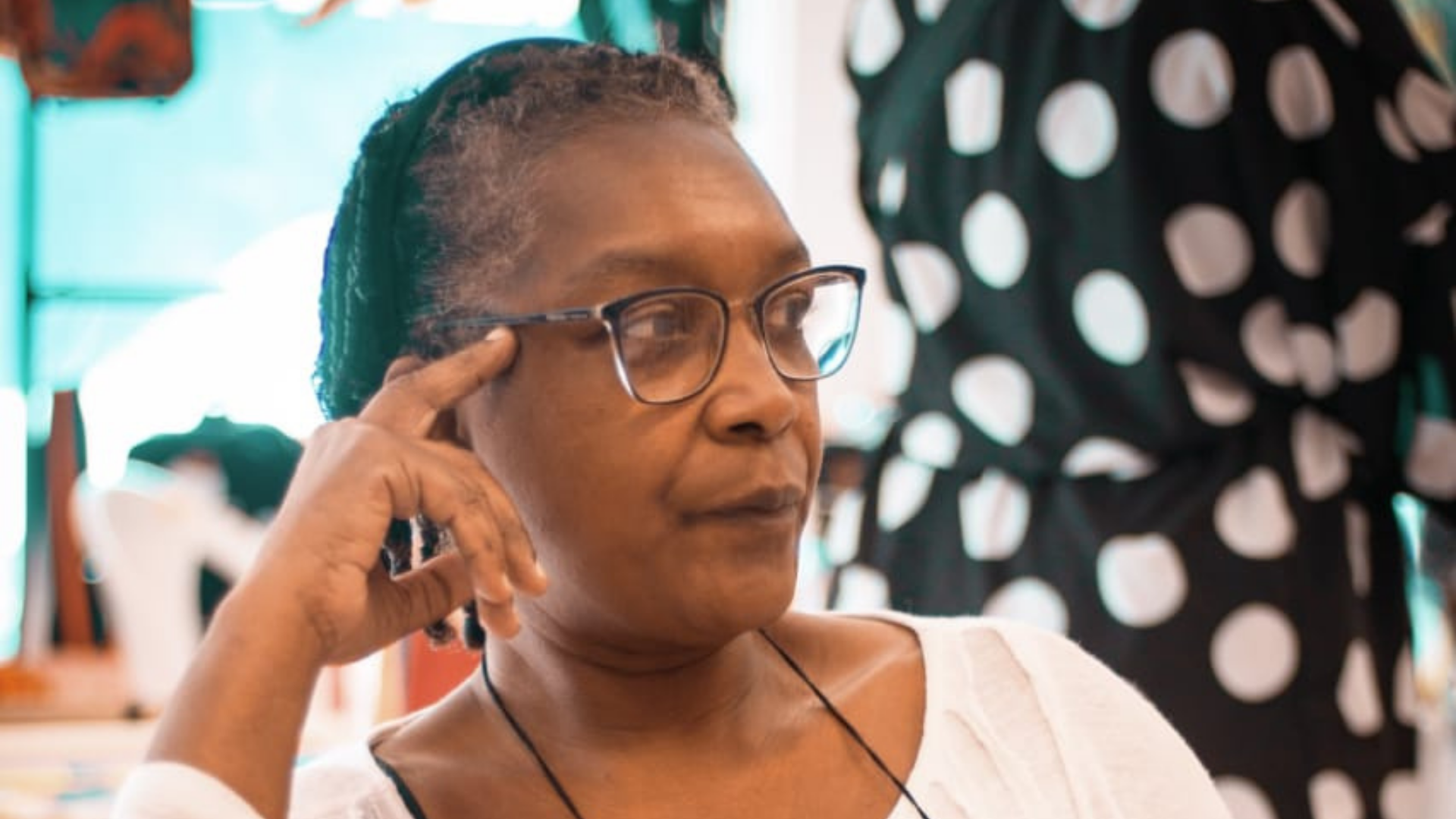 Cláudia usa óculos de grau, pele negra, blusa branca e cabelo crespo grisalho.