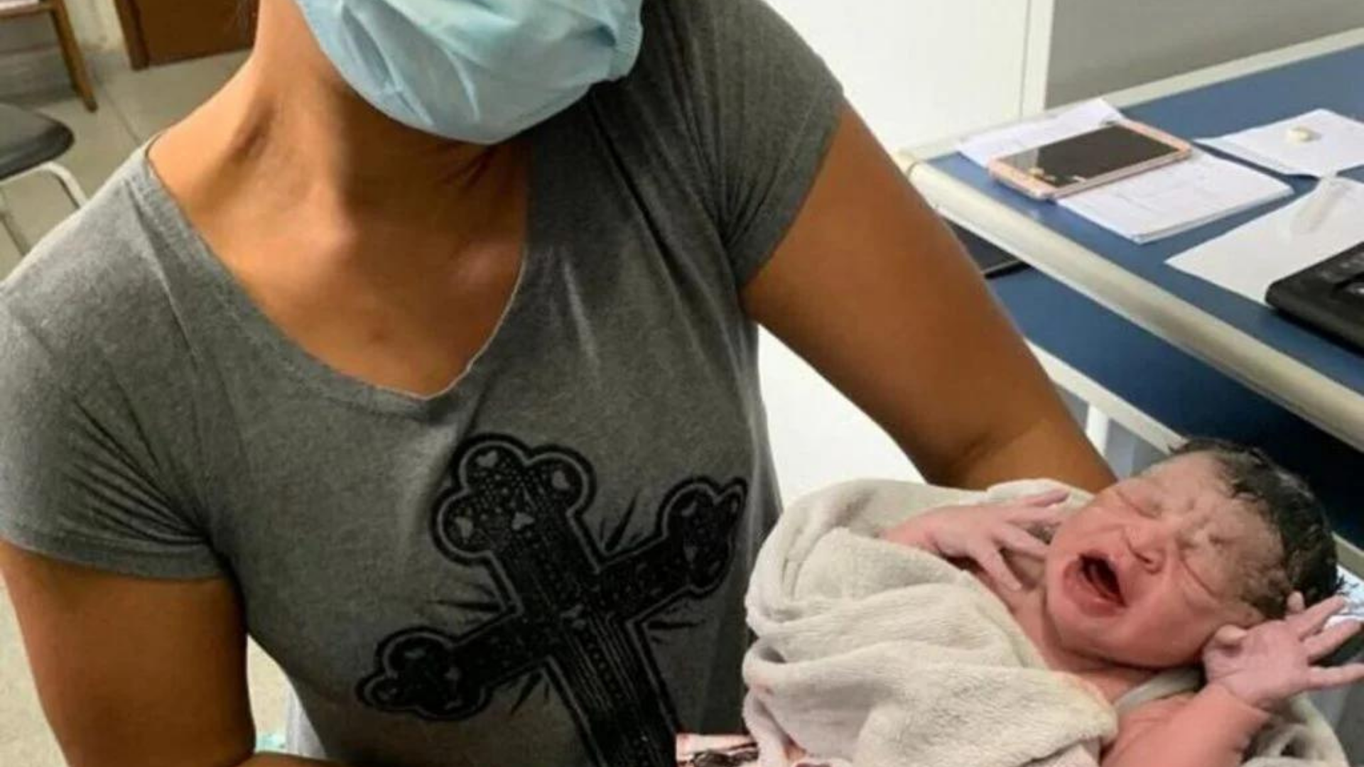 Bebê nasce em ponto de apoio à tragédia em Petrópolis. Na foto, a bebê aparece chorando enrolada em leçóis com uma mulher, que não aparece na foto a segurando.