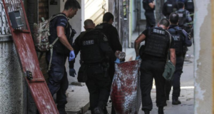 Foto de policiais com farda preta carregando um corpo dentro de um pano em uma rua no Rio de Janeiro