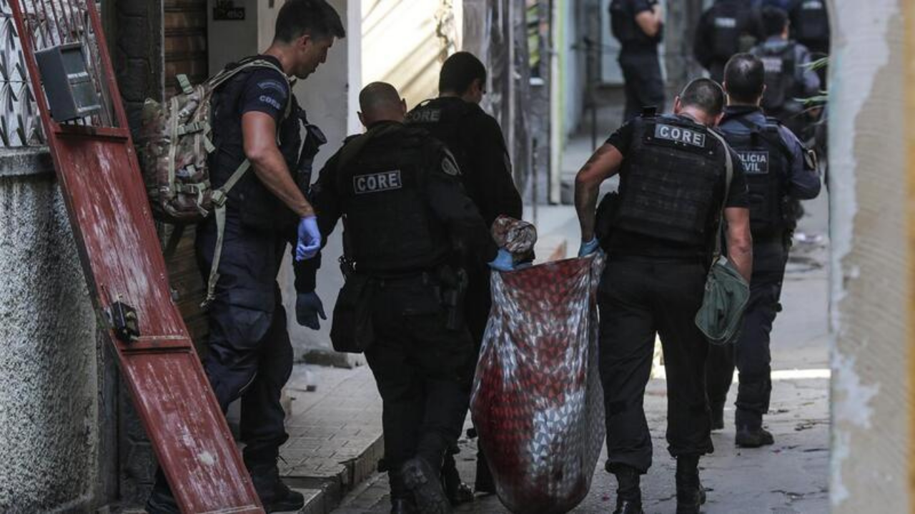 Foto de policiais com farda preta carregando um corpo dentro de um pano em uma rua no Rio de Janeiro