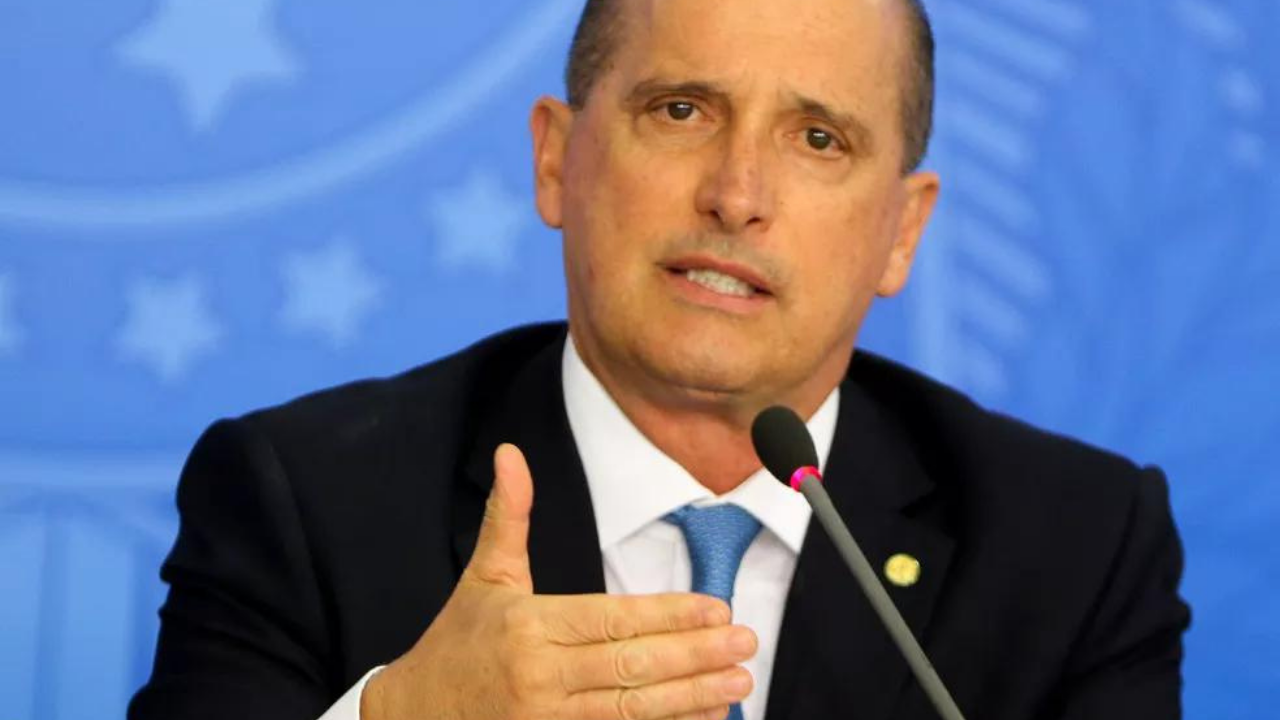 Foto de Onyx Lorenzoni falando e gesticulando com as mãos. No fundo há um painel azul.