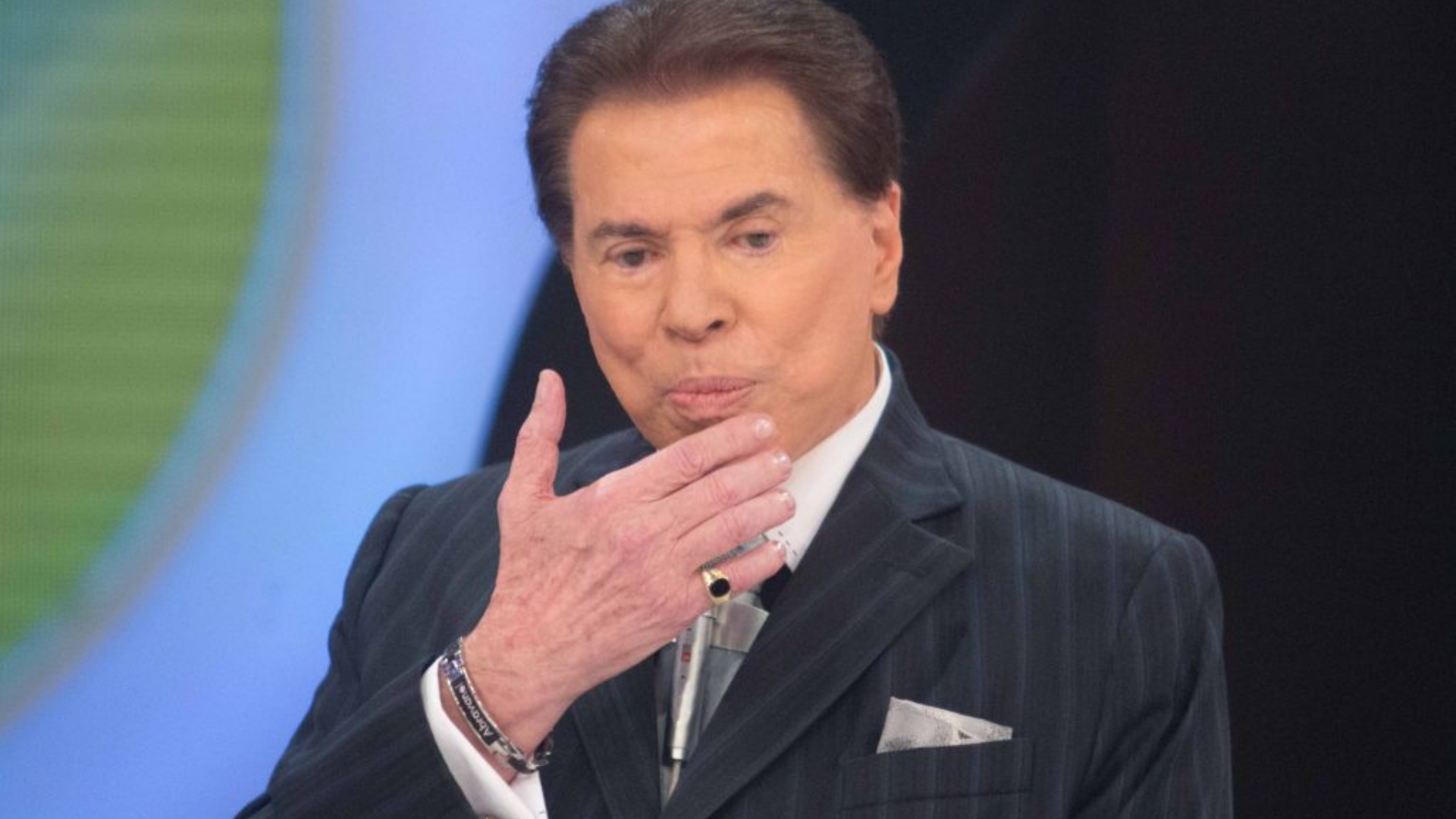 Juíza impõe derrota a Silvio Santos. Ele usa terno preto, anel no dedo mindinho, cabelo preto e pele branca.