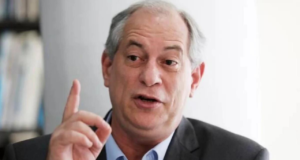 Ciro Gomes com o dedo indicador d amãe direita levantado, ele usa terno preto e tem cabelos brancos.