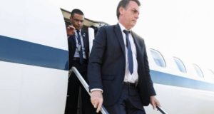 Após fracasso em viagem à Europa, Bolsonaro promete visita à América Central. Ele usa terno preto e gravata azul, está descendo de um avião.