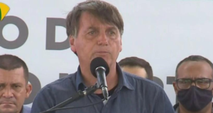 Bolsonaro fala em microfone.O cabelo dele está bagunçado, ele usa uma camisa azul.