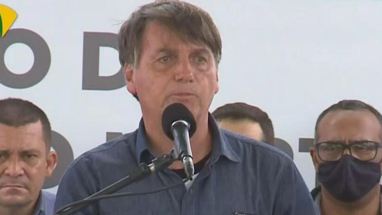 Bolsonaro fala em microfone.O cabelo dele está bagunçado, ele usa uma camisa azul.