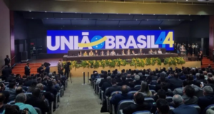 União Brasil quer apoiar de Lula a Bolsonaro. Foto de evento com uma grande logo do partido em um telão.