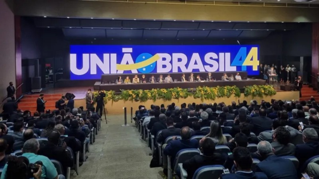União Brasil quer apoiar de Lula a Bolsonaro. Foto de evento com uma grande logo do partido em um telão.