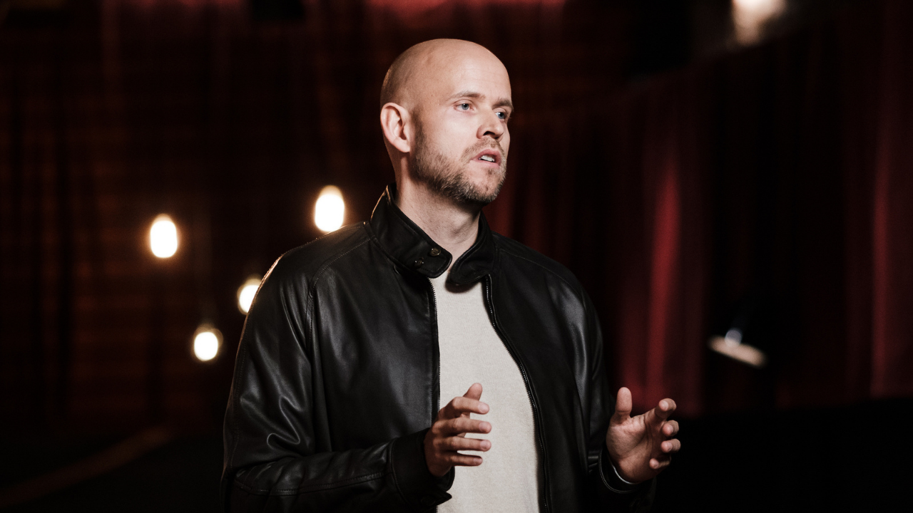 Daniel EK com camisa branca e jaqueta preta. Ele usa barba e é calvo