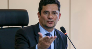 Foto de Sergio Moro usando terno preto e gravada azul. Ele não tem barba e fala ao microfonene