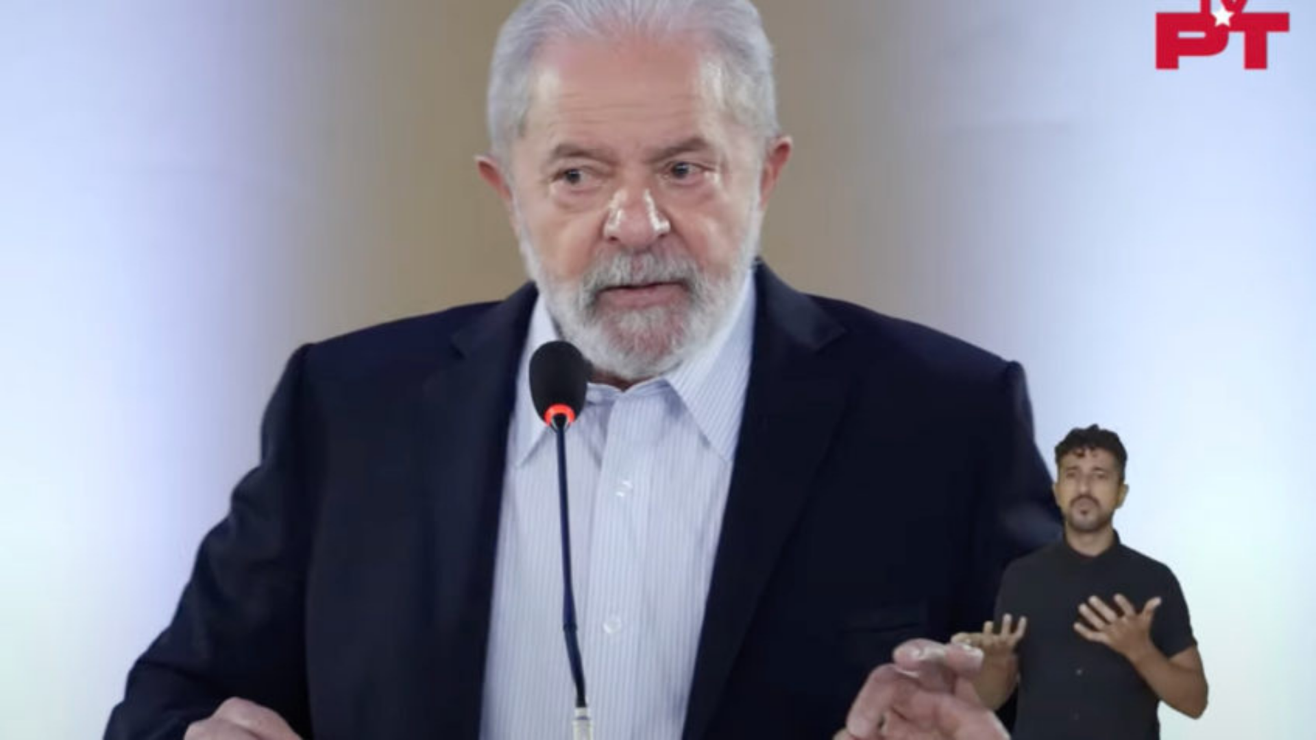 Lula diz que Bolsonaro só sabe "mentir e fazer propaganda de armas". Ele usa terno cinza e tem olhar confiante. 