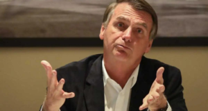 Foto de Bolsonaro usando terno cinza e fazendo sinal com os dois braços como se não subesse de alguma coisa.