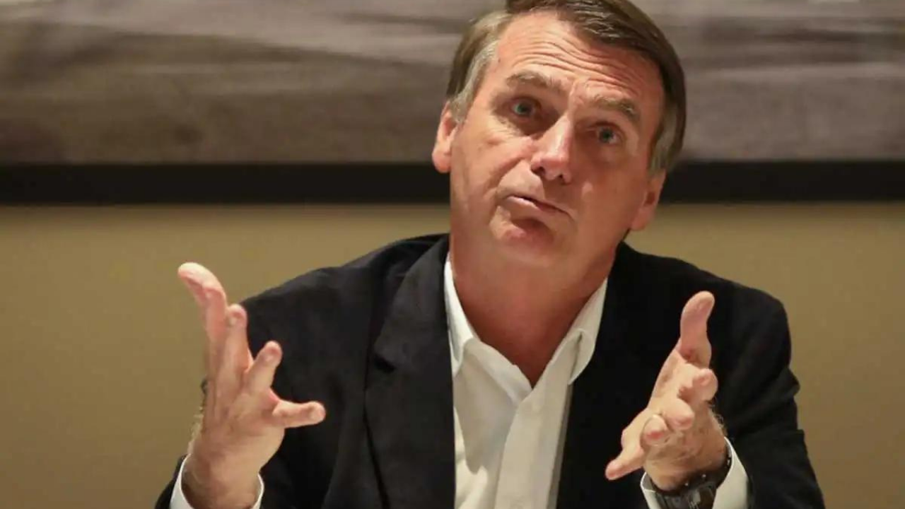 Foto de Bolsonaro usando terno cinza e fazendo sinal com os dois braços como se não subesse de alguma coisa.