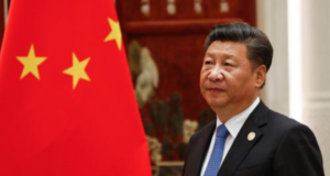 Presidente da china envia mensagem de solidariedade às vítimas de tragédia. Ele está aparecendo de lado na imagem, usa terno preto, cabelo preto e à frente há uma bandeira da China.