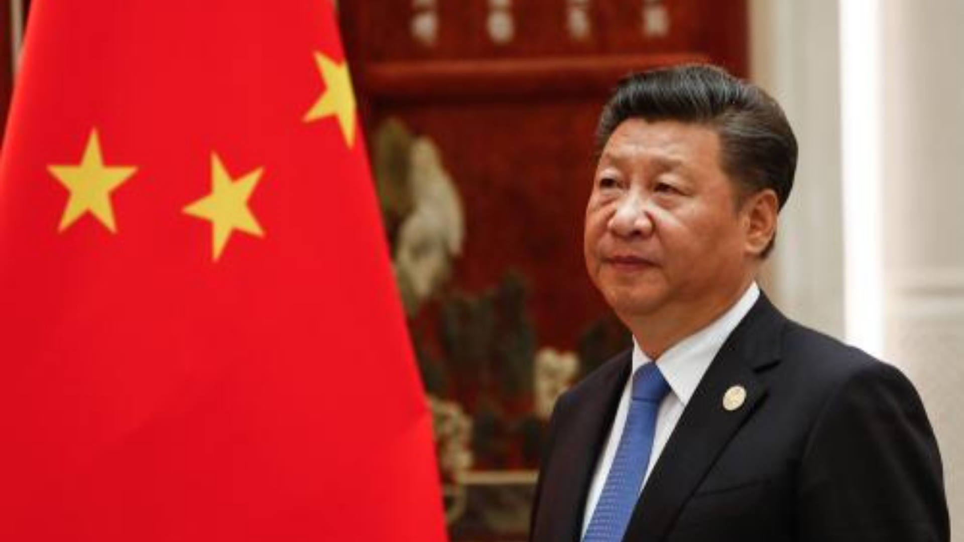 Presidente da china envia mensagem de solidariedade às vítimas de tragédia. Ele está  aparecendo de lado na imagem, usa terno preto, cabelo preto e à frente há uma bandeira da China.