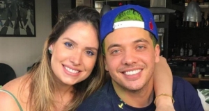 Foto de Wesley Safadão, sorrindo, com camisa azul e cabelo verde, ele usa um bone azul. Do lado esquerdo da foto está a companheira dele, Thyane Dantas, é loira, está sorrindo, ambos tem pele branca.