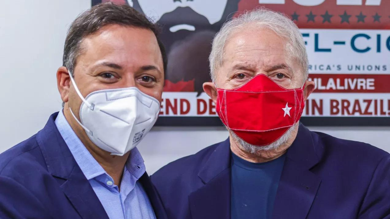 Foto de Andre Cecliano e o ex-presidente Lula. Ambos usam ternos azuis, usam máscara. Ceciliano tem cabelo castanho e pele branca.