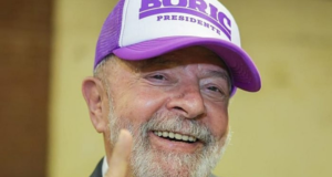 Lula avisa que não irá ao Chile para posse de Boric. O ex-presidente está sorrindo, com um terno preto, e usa um boné com o nome Boric".