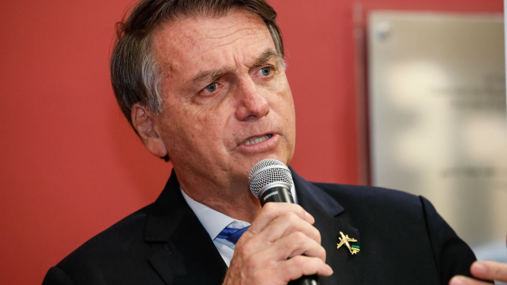 Bolsonaro é tratado pela imprensa russa como aliado de Putin. Ele aparece em foto falando para alguém, com expressão marcante.