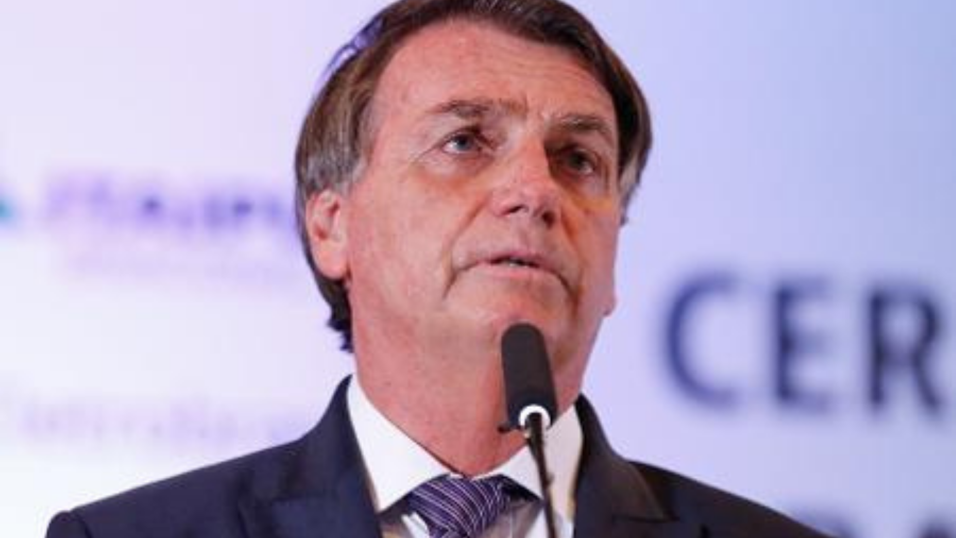 Rejeição de Bolsonaro dispara na web após Rússia invadir Ucrânia. Presidente aparece com expressão de preocupação e fala ao microfone eme evento. Fundo desfocado.