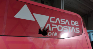 Ônibus com jogadores do Bahia sofre atentado à bomba. Foto do ônibus na cor vermelha e buraco com marca da bomba.