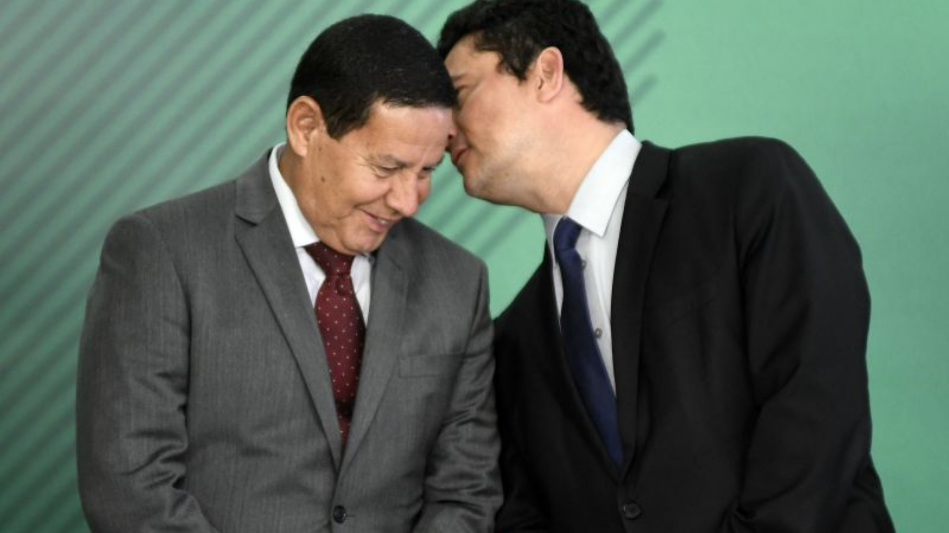 Moro se derrete por Mourão: "Voz sensata na República". Moro fala ao ouvido de Mourão, ele usa terno preto e Mourão terno cinza.