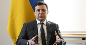 Presidente da Ucrânia diz que país foi abandonado. Foto de Zelensky usando terno cinza, pelo branca, cabelos e gravata preta. Ele gesticula com as mãos, bandeira da Ucrânia ao fundo.