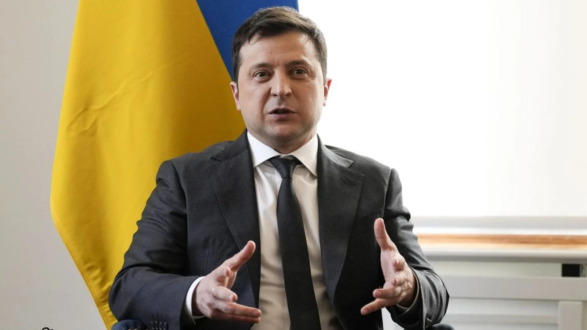 Presidente da Ucrânia diz que país foi abandonado. Foto de Zelensky usando terno cinza, pelo branca, cabelos e gravata preta. Ele gesticula com as mãos, bandeira da Ucrânia ao fundo.