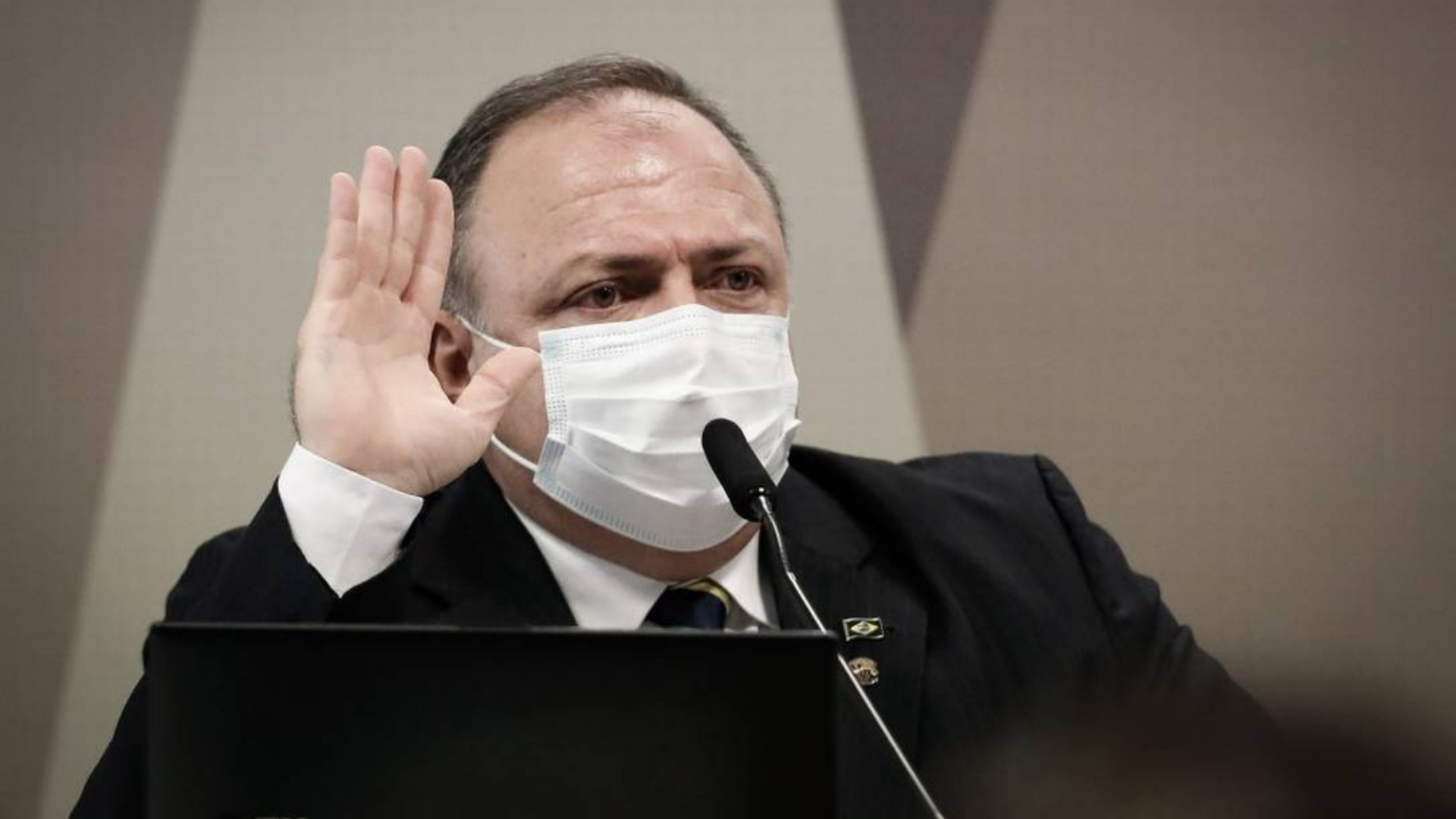 Pazuello decide trocar farda por eleições. Foto do ex-ministro com terno azul e máscara cirúrgica branca.