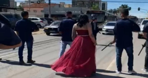 Homens com fuzis param trânsito para dama de vermelho passar. Mulher usando vestido vemelho para no meio da rua junto com homens armados com fuzis.