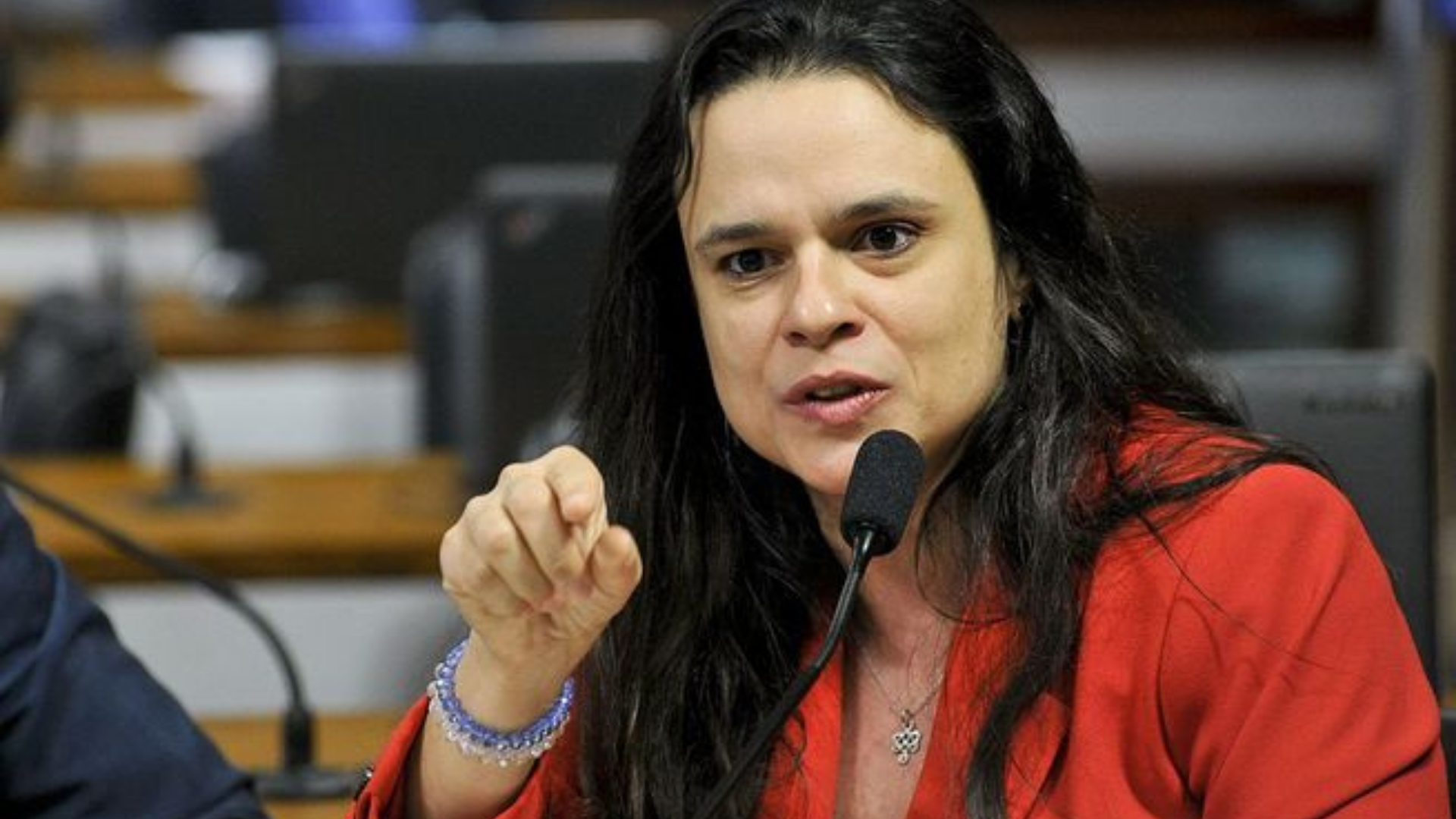 Janaina Paschoal sobre Bolsonaro não apoia-la ao Senado: "Tem medo de mim". Ela tem expressão facial de raiva, está apontando o dedo indicador direito, tem os cabelos soltos e usa um vestido laranja.