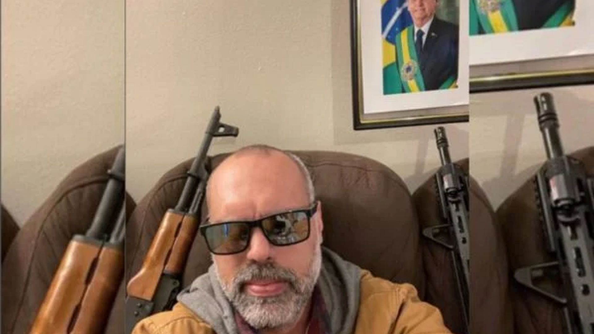 Allan dos Santos, em foto com armas atrás e uma foto de Bolsonaro