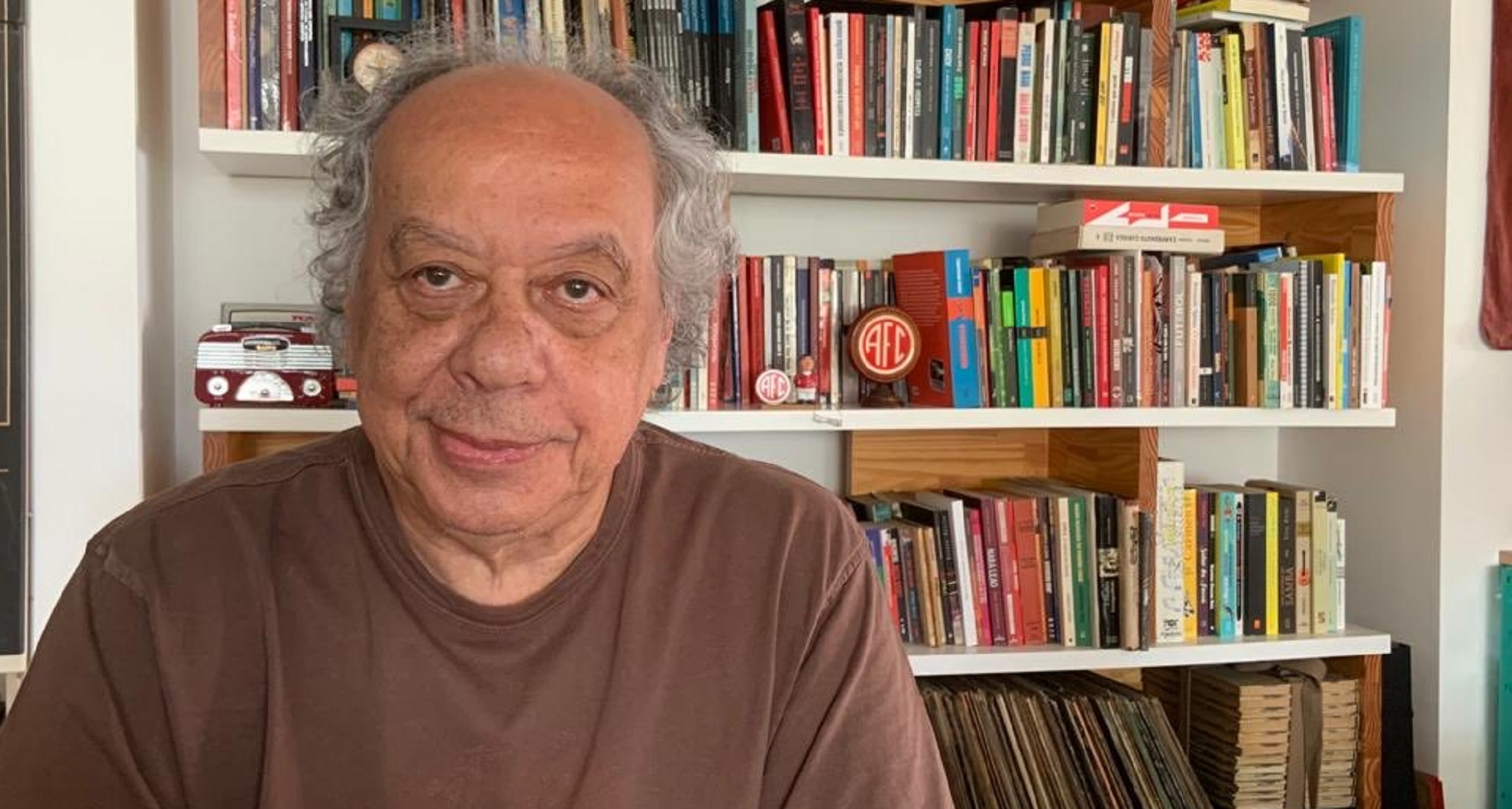 José Trajano sentado à frente da sua biblioteca: José Trajano está com Covid-19