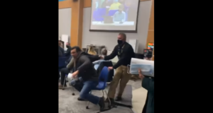 Segurança puxando homem sem máscara pelo casaco enquanto ele resiste e se mantém sentado na cadeira.