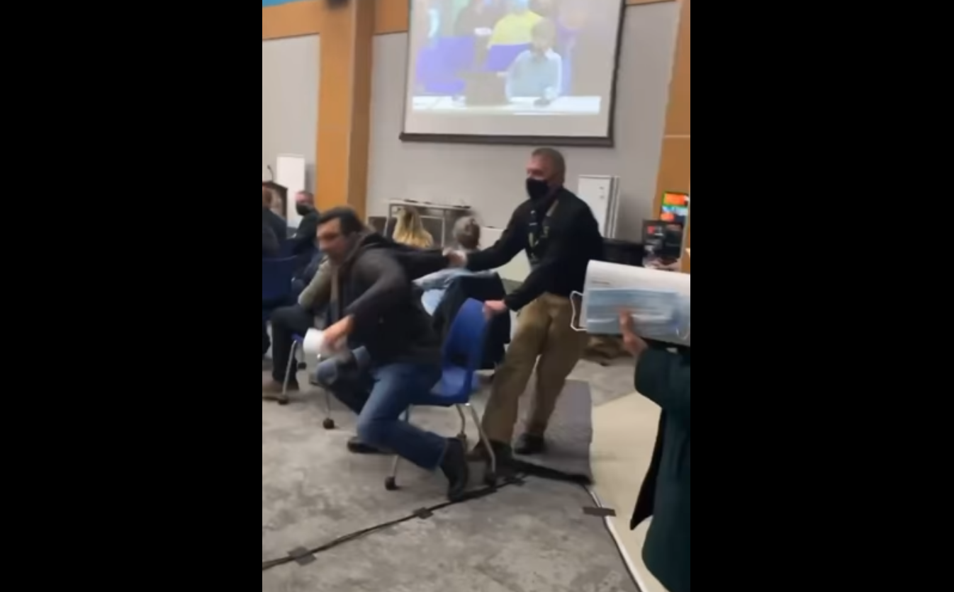 Segurança puxando homem sem máscara pelo casaco enquanto ele resiste e se mantém sentado na cadeira.