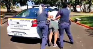 Mulher negacionista sendo conduzida à viatura após tentar resistir à prisão, em Araraquara. Ela mantém as mãos nas costas, enquanto é levada por dois policiais.