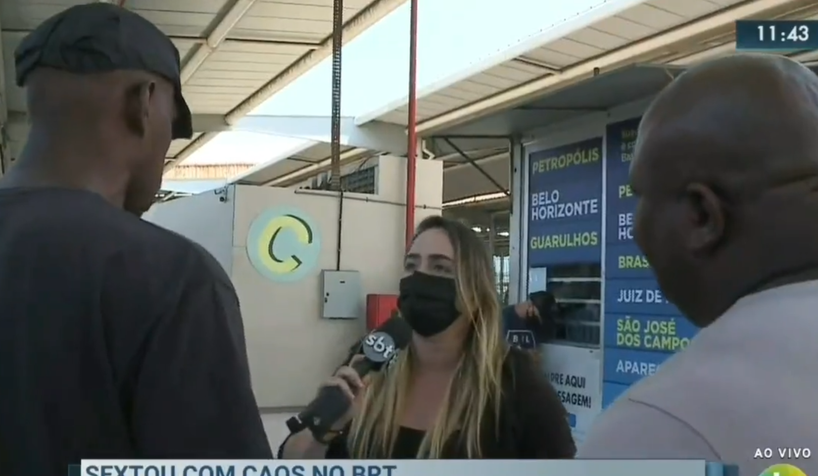 A repórter está no centro da imagem, com o microfone na mão, enquanto dois homens ficam entre ela e a câmera, tentando impedir o trabalho da reportagem.