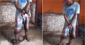Homem negro, em pé, acorrentado nas mãos e nos pés.