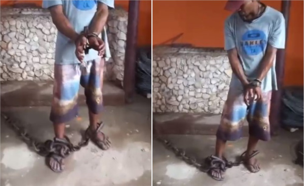 Homem negro, em pé, acorrentado nas mãos e nos pés.