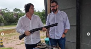 Mario Frias em um clube de tiro segurando uma arma escopeta. Ao seu lado, o vereador Paulo Chuchu, de São Bernardo do Campo.