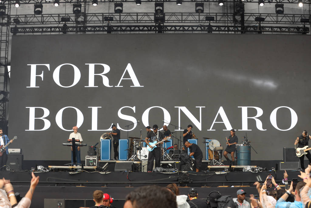 Mensagem "Fora Bolsonaro" em projeção no palco do festival musical Lollapalooza, enquanto uma banda se apresenta.