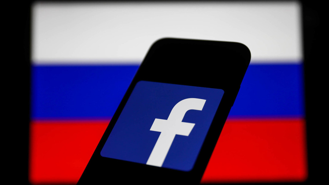 Imagem ilustrativa da bandeira da Rússia atrás de um celular com o símbolo do Facebook.